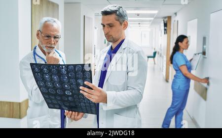 Deux médecins analysant l'IRM du cerveau du patient tout en se tenant dans le couloir de la clinique moderne pendant la journée de travail. le travail d'équipe médical Banque D'Images