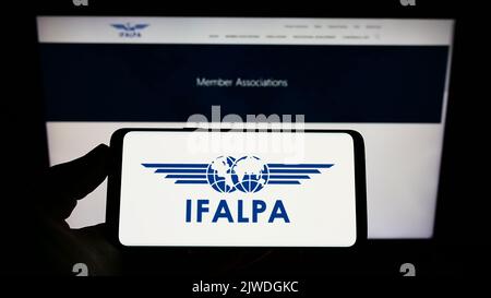 Personne tenant un smartphone avec le logo de l'association pilote internationale IFALPA à l'écran devant le site. Mise au point sur l'affichage du téléphone. Banque D'Images