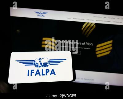 Personne tenant un téléphone portable avec le logo de l'association pilote internationale IFALPA à l'écran en face de la page web. Mise au point sur l'affichage du téléphone. Banque D'Images