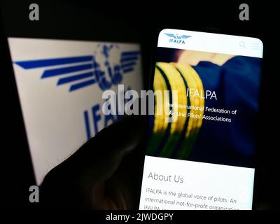Personne tenant un téléphone portable avec le site Internet de l'association internationale pilote IFALPA sur l'écran devant le logo. Concentrez-vous sur le centre de l'écran du téléphone. Banque D'Images