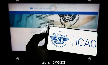 Personne tenant un téléphone portable portant le logo de l'Organisation de l'aviation civile internationale (OACI) à l'écran devant la page Web. Mise au point sur l'affichage du téléphone. Banque D'Images