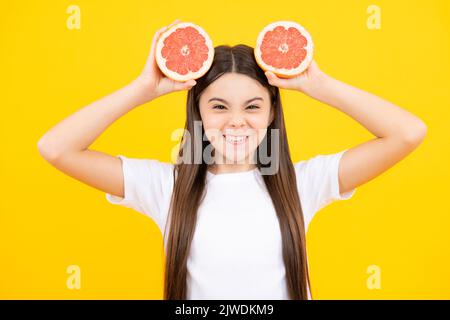 Visage amusant. Adolescente portant un pamplemousse sur fond jaune. Banque D'Images