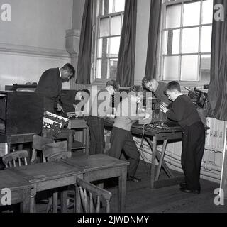 1960s, historique, jeunes garçons dans une salle de classe primaire, avec un professeur de sexe masculin, prenant part à une leçon d'électronique de base, jouant avec le câblage sur les anciens émetteurs radio et téléviseurs, Royaume-Uni. L'électronique amateur était un passe-temps populaire à cette époque, avec un certain nombre de magazines destinés au marché, y compris l'électronique populaire, publié pour la première fois en 1954 pour un public de amateurs et d'expérimentateurs d'électronique. En 1963, elle a été diffusée en 400 000 et était le plus grand magazine électronique au monde pour les amateurs de technologie. Banque D'Images