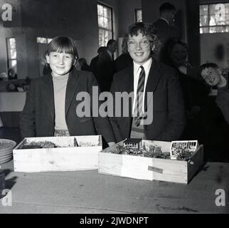 1960s, prix historiques... deux écolières souriantes debout pour une photo avec leurs jardins miniatures qu'elles ont créés pour un concours scolaire. Banque D'Images