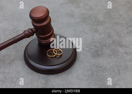 Thème droit. Jugez les anneaux de mariage de gavel sur fond gris en pierre de béton. Procédure de divorce. Maillet de juge qui décide du divorce de mariage, de l'accord matrimonial, des légalités du divorce Banque D'Images