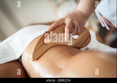 Une femme thérapeute effectue une maderothérapie sur les jambes d'une femme à l'aide d'une spatule de massage en bois Banque D'Images