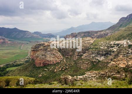 Des nuages orageux se rassemblent au-dessus d'une vallée entourée de falaises et de montagnes bleues lointaines dans les montagnes du Drakensberg Banque D'Images