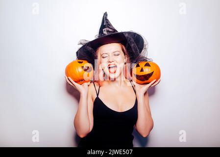 Belle fille sorcière tient une citrouille dans ses mains. Femme célébrant halloween, joie et sourire sur son visage. Vacances d'automne et fêtes Banque D'Images