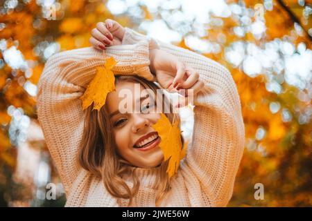 Photo portrait d'une fille dans un chandail blanc, la blonde tient une feuille dans sa main. Jolie femme dans le parc en automne rires, joie, sourire. Fashio d'automne Banque D'Images