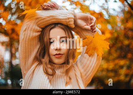 Photo portrait d'une fille dans un chandail blanc, la blonde tient les feuilles dans ses mains. Jolie femme dans le parc en automne. Mode et style automnaux. Chaud Banque D'Images