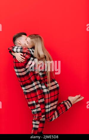 Bonne Saint Valentin. Jeune couple dans le même pyjama est embrassant et embrassant sur fond rouge.l'homme et la femme dans l'amour aiment dépenser tim Banque D'Images