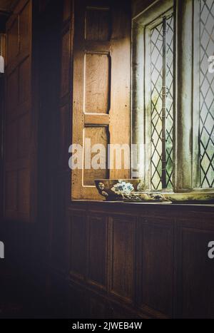 La lumière brille par une fenêtre au plomb dans une salle lambrissée en bois d'un manoir anglais. Banque D'Images