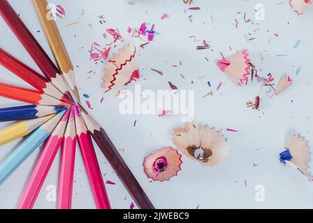 Un gros plan de crayons de couleur aiguisés avec des copeaux, sont disposés en demi-cercle sur la surface blanche Banque D'Images