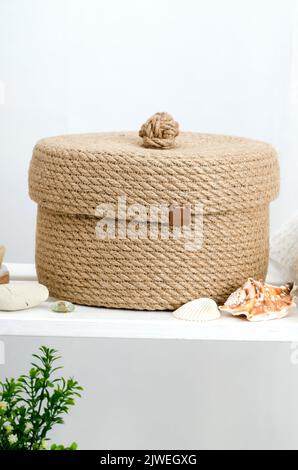 Panier en jute tricoté à la main avec un couvercle dans la salle de bains sur une étagère en bois blanc. Banque D'Images