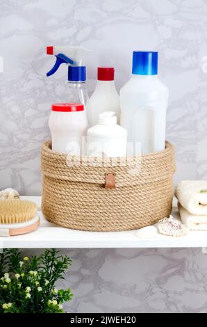 Panier en jute tricoté à la main avec un couvercle avec des détergents et des serviettes dans la salle de bains sur un rack en bois blanc. Banque D'Images