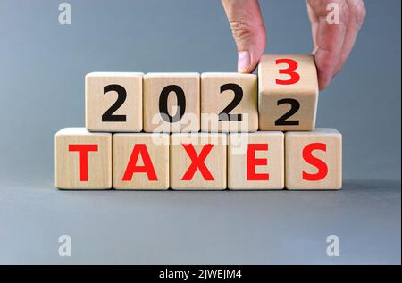 symbole 2023 taxes nouvel an. Homme d'affaires transforme un cube en bois et change les mots impôts 2022 en impôts 2023. Magnifique fond gris de table, Copy spa Banque D'Images