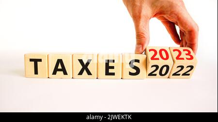 symbole 2023 taxes nouvel an. Homme d'affaires transforme un cube en bois et change les mots impôts 2022 en impôts 2023. Beau tableau blanc fond blanc, copie s Banque D'Images