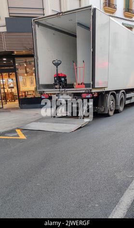 Camion semi-remorque déchargeant des marchandises au centre-ville. Le chariot est équipé d'une rampe de levage Banque D'Images