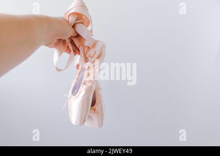 Ballerina danseuse main tenant de nouvelles chaussures de ballet beige pastel avec ruban de satin isolé sur fond blanc. Ballerine classique pointe chaussures pour l'entraînement de danse. Concept d'école de ballet. Copier l'espace Banque D'Images