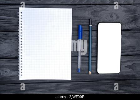 Vue de dessus de la tasse à café et du bloc-notes avec un stylo et un smartphone vide sur la table en bois. Banque D'Images