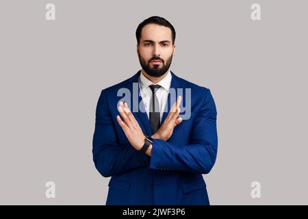 Non, c'est la fin. Homme barbu croisant les mains, avertissement gestuelle ou interdiction, ce qui signifie arrêt de finition, portant le costume de style officiel. Prise de vue en studio isolée sur fond gris. Banque D'Images