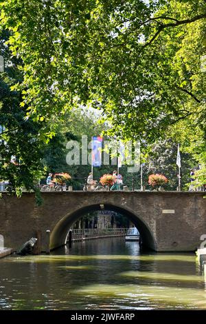 Utrecht, pays-Bas - août 2022 : personnes traversant un vieux pont en pierre avec des paniers de fleurs sur l'un des canaux de la ville Banque D'Images