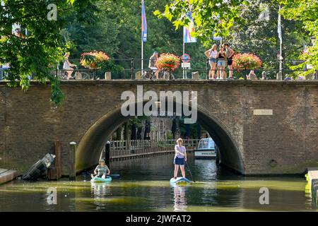 Utrecht, pays-Bas - août 2022 : deux personnes pagayez sous un vieux pont en pierre avec des paniers de fleurs sur l'un des canaux de la ville Banque D'Images