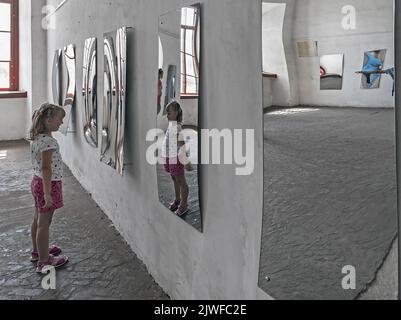 La jeune fille non identifiée regardant son image dans le miroir déformé de la salle des miroirs à Dubno, Ukraine Banque D'Images