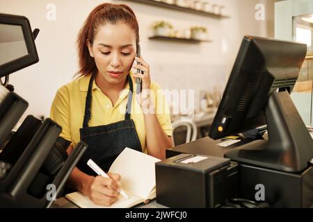 La serveuse du café accepte la commande par téléphone et prend des notes dans le bloc-notes Banque D'Images