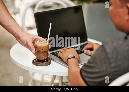 Image en gros plan du serveur mettant un verre de café glacé sur une table devant le client travaillant sur un ordinateur portable Banque D'Images