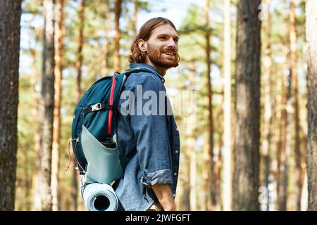Jeune homme souriant avec randonnée à dos dans la forêt en été Banque D'Images