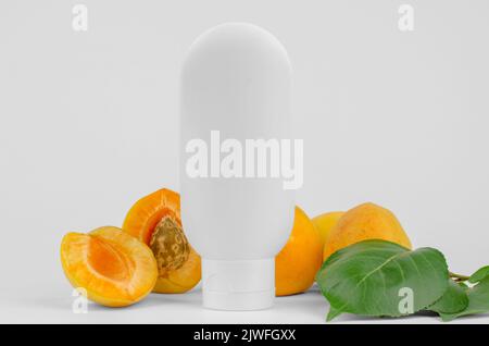 Vider le tube en plastique blanc et les abricots frais sur fond blanc. Maquillage de marque de cosmétiques naturels pour hydratant, lotion pour le corps, lait pour le corps Banque D'Images