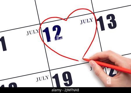 12th jour de juillet. Une main de femme dessinant un coeur rouge à la date du calendrier du 12 juillet. Le coeur comme symbole de l'amour. Mois d'été. Jour de l'année co Banque D'Images