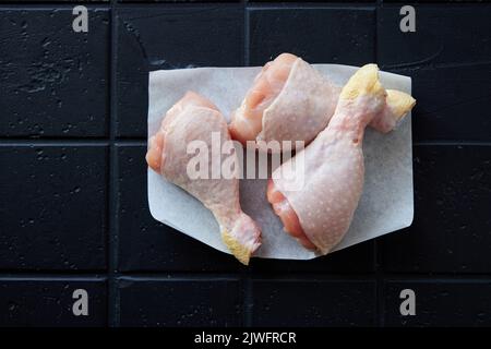 Vue de dessus tas de pilons de poulet frais avec la peau placée sur fond noir clair dans la cuisine légère pendant la préparation de la cuisson Banque D'Images