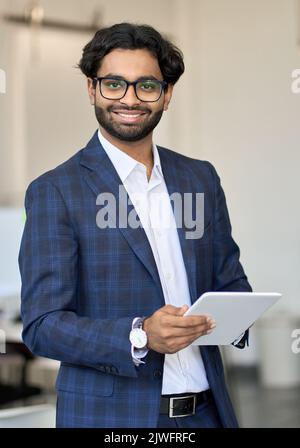 Jeune homme d'affaires indien souriant portant un costume tenant une tablette, vertical. Banque D'Images