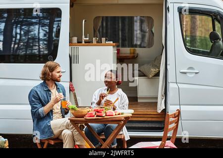 Jeune couple multiethnique assis à table et déjeuner ensemble pendant le pique-nique dans la forêt Banque D'Images