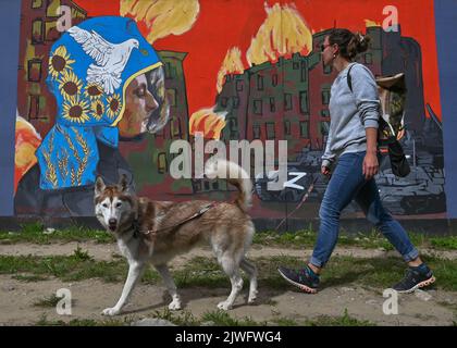 GDANSK, POLOGNE. 05 septembre 2022. Une jeune femme avec un chien passe devant une fresque pro-ukrainienne et anti-guerre créée par l'artiste polonaise Maria Morawska. Près de 30 peintures murales anti-guerre ont été peintes sur le mur à l'arrêt PKM Gdansk Jasien Mapka dans le cadre du projet "en solidarité avec l'Ukraine" lancé par le PKM et l'Académie des beaux-arts de Gdansk. Beaucoup de ces peintures murales sont liées au conflit russo-ukrainien de 2022. Crédit : ASWphoto/Alamy Live News Banque D'Images