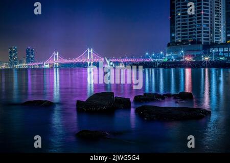 Les rochers d'une rivière avec le pont de diamant illuminé de la ville de Busan en arrière-plan avec des bâtiments modernes en Corée du Sud Banque D'Images