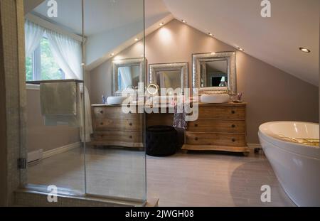 Salle de bains principale avec armoires en bois et miroirs encadrés d'argent à l'intérieur d'une luxueuse maison. Banque D'Images