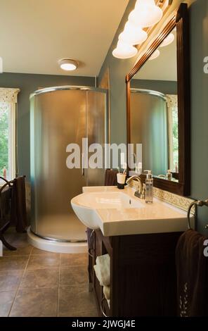 Salle de bains principale avec lavabo en porcelaine et cabine de douche en verre à l'intérieur d'une maison de style cottage. Banque D'Images
