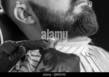 Homme taillé sa barbe avec un rasoir électrique dans un salon de coiffure. Image en noir et blanc. Banque D'Images