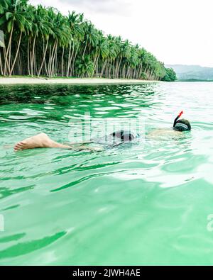 Homme snorkeling dans la mer d'eau vert cristal en Asie du Sud-est. En arrière-plan, vous pouvez voir la plage et les palmiers. Endroit paradisiaque Banque D'Images