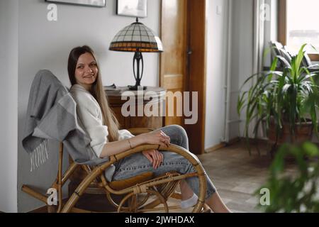 Jeune femme assise sur une chaise à bascule. Ambiance chaleureuse, vie lente, personnes se reposer. Intérieur de maison vintage. Personne sur un fauteuil à l'ancienne Banque D'Images