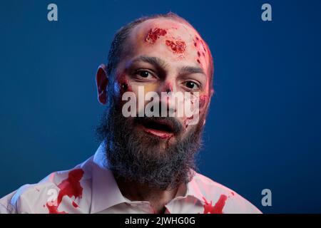 Portrait d'un zombie terrifiant mort-mort posant avec des cicatrices sanglantes et un costume d'halloween effrayant à l'air dangereux et apocalyptique. Horreur agressif monstre mortel cadavre mangeant cerveau. Banque D'Images