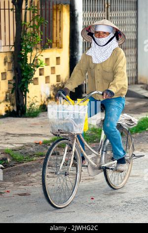 Femme vietnamienne à vélo, portant un chapeau de bambou et un masque facial, Hai Phong, Vietnam Banque D'Images