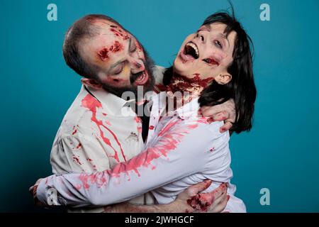 Cerveau mangeant halloween zombies embrassant sur fond bleu, agissant agressif et effrayant. Couple de monstres crues avec du sang et des rayures sales partageant le hug sur l'appareil photo, des blessures sanglantes. Banque D'Images