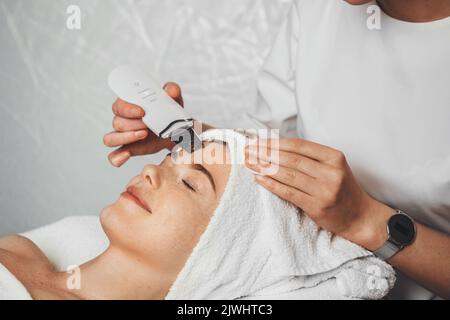 Gros plan sur le visage de la femme lors de la procédure de peau par ultrasons au spa. Gommage du visage par ultrasons. Nettoyage du visage par ultrasons à Banque D'Images