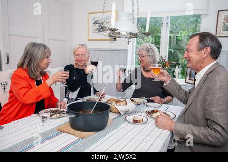 Groupe de personnes ayant dîner à la maison. Des amis heureux assis autour de la table à manger manger de la nourriture et de parler Banque D'Images