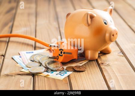 Fiche électrique, euro Money et piggy Bank sur table en bois. Concept d'augmentation des prix de l'électricité. Banque D'Images