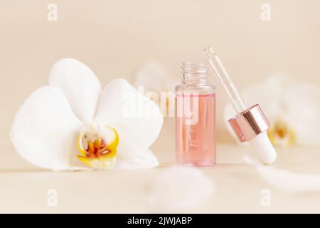 Flacon de Dropper ouvert rose clair avec sérum et bouchon de pipette près des fleurs d'orchidées blanches sur beige clair, gros plan, espace de copie. Produit cosmétique pour le soin de la peau Banque D'Images